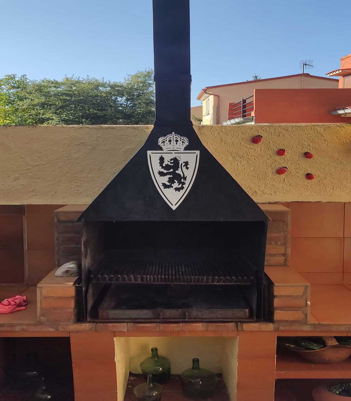 Escudos de fútbol en blanco para pared: escudo de Real Zaragoza aparece colocado sobre una estructura de barbacoa o chimenea exterior. Es un ejemplo perfecto de cómo un escudo en blanco puede funcionar fuera del salón típico